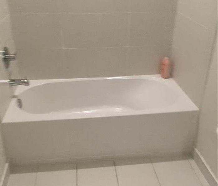 White bathtub with white tile and a pink shampoo bottle. 