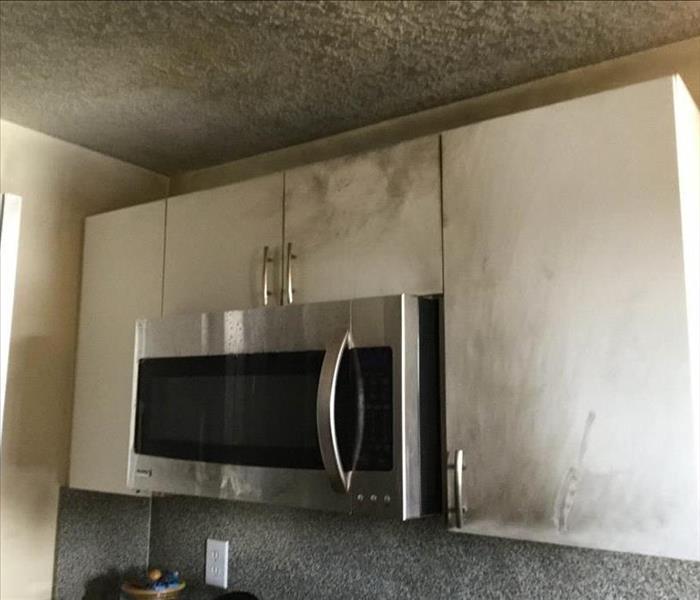 White cabinets and a microwave covered in soot stains. 