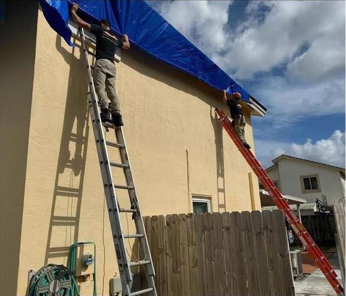 servpro technicians tarping a roof of a house