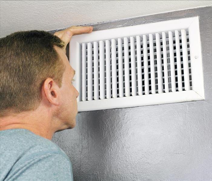 Mature man examining an outflow air vent grid and duct to see if it needs cleaning.