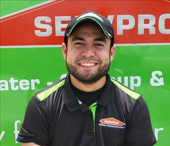 Male employee with black hair smiling in front of a green background